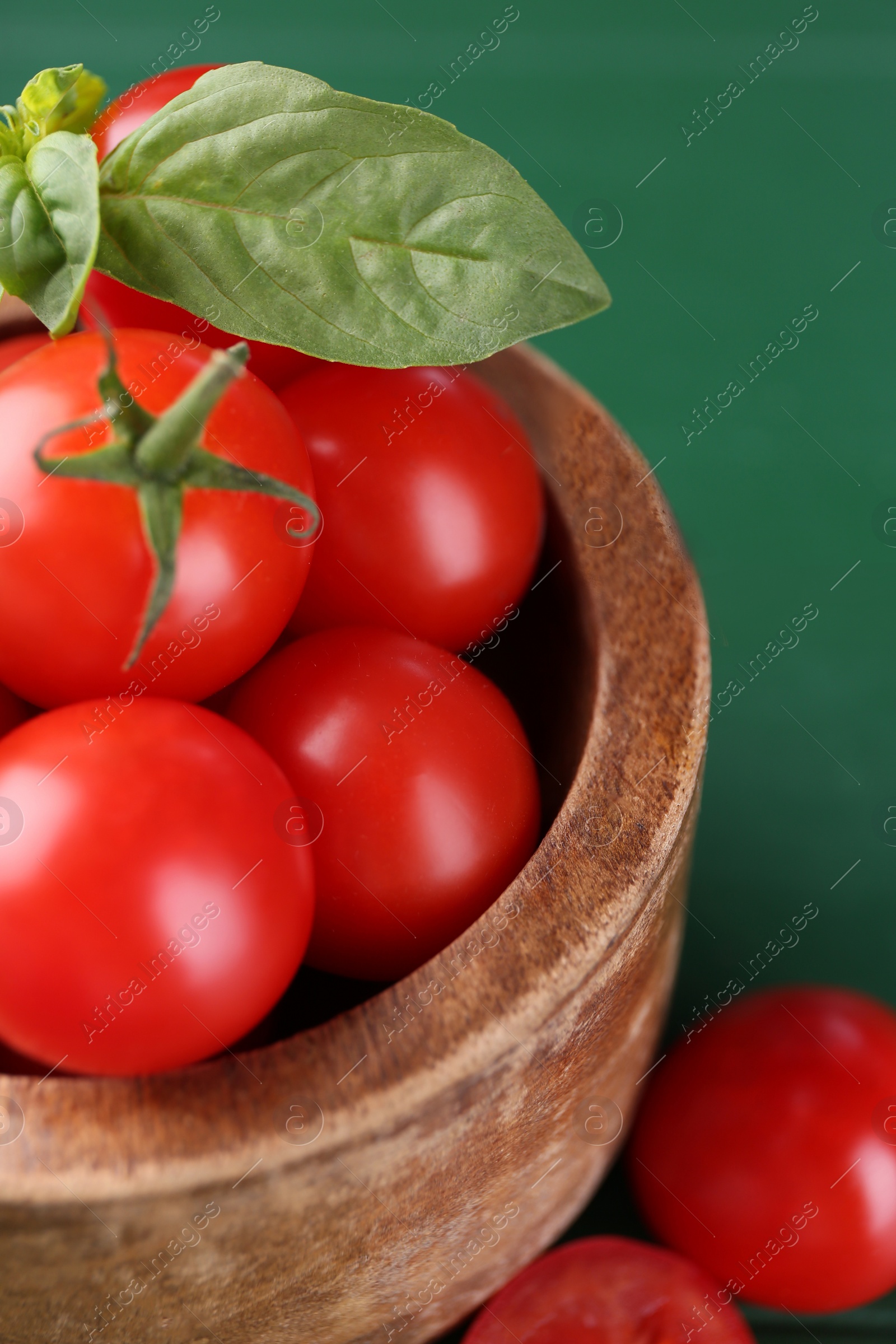 Photo of Ripe tomatoes in wooden bowl on green table, closeup