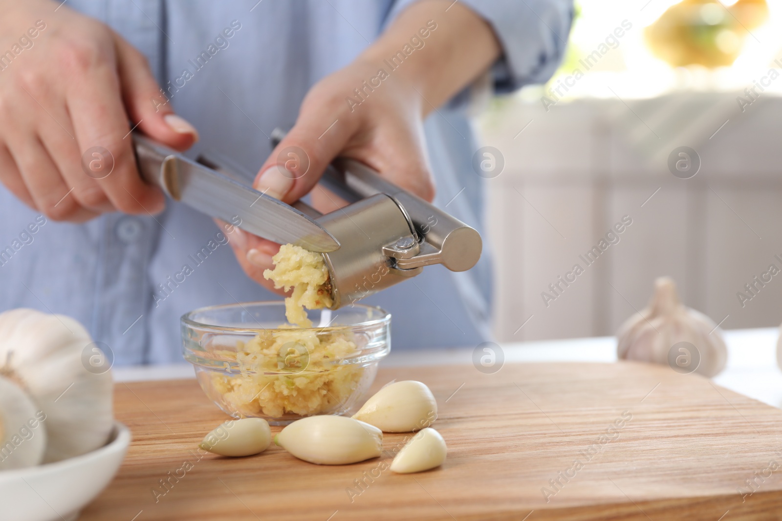 Photo of Woman squeezing garlic with press at wooden table indoors, closeup