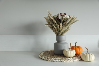 Beautiful bouquet of dry flowers and small pumpkins on white table near light wall, space for text