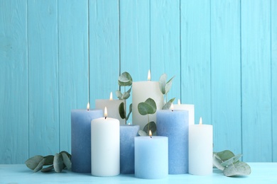 Photo of Set of burning candles with eucalyptus on table against light blue wooden background