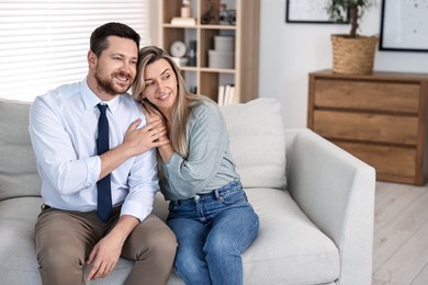 Photo of Happy couple sitting on sofa at home, space for text