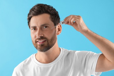 Smiling man applying cosmetic serum onto his face on light blue background