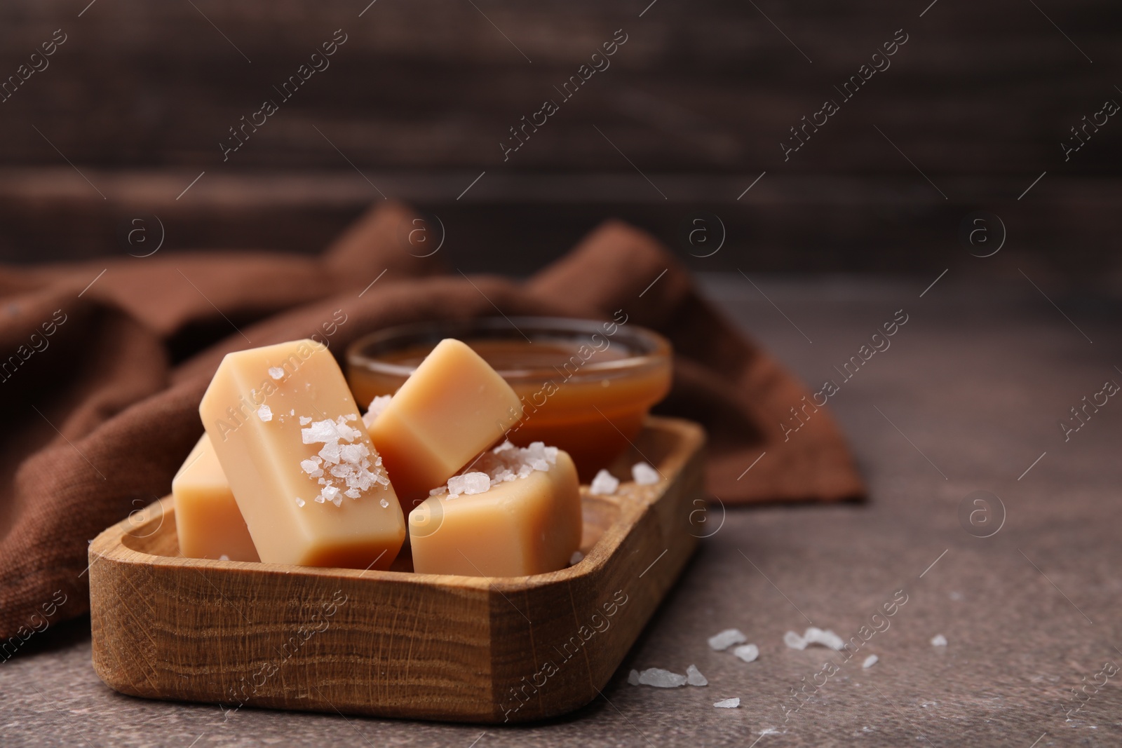 Photo of Yummy caramel candies, sauce and sea salt on brown table, closeup. Space for text