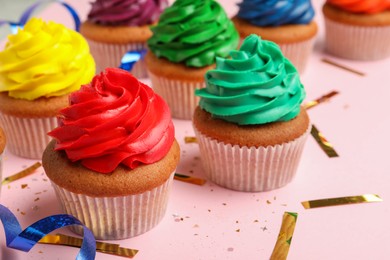 Photo of Many delicious colorful cupcakes and confetti on pink table, closeup