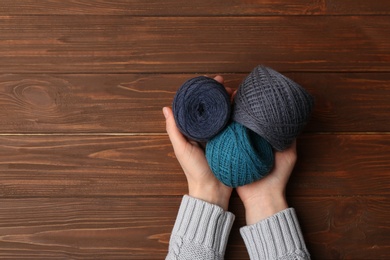 Photo of Woman holding clews of threads on wooden background, top view. Space for text