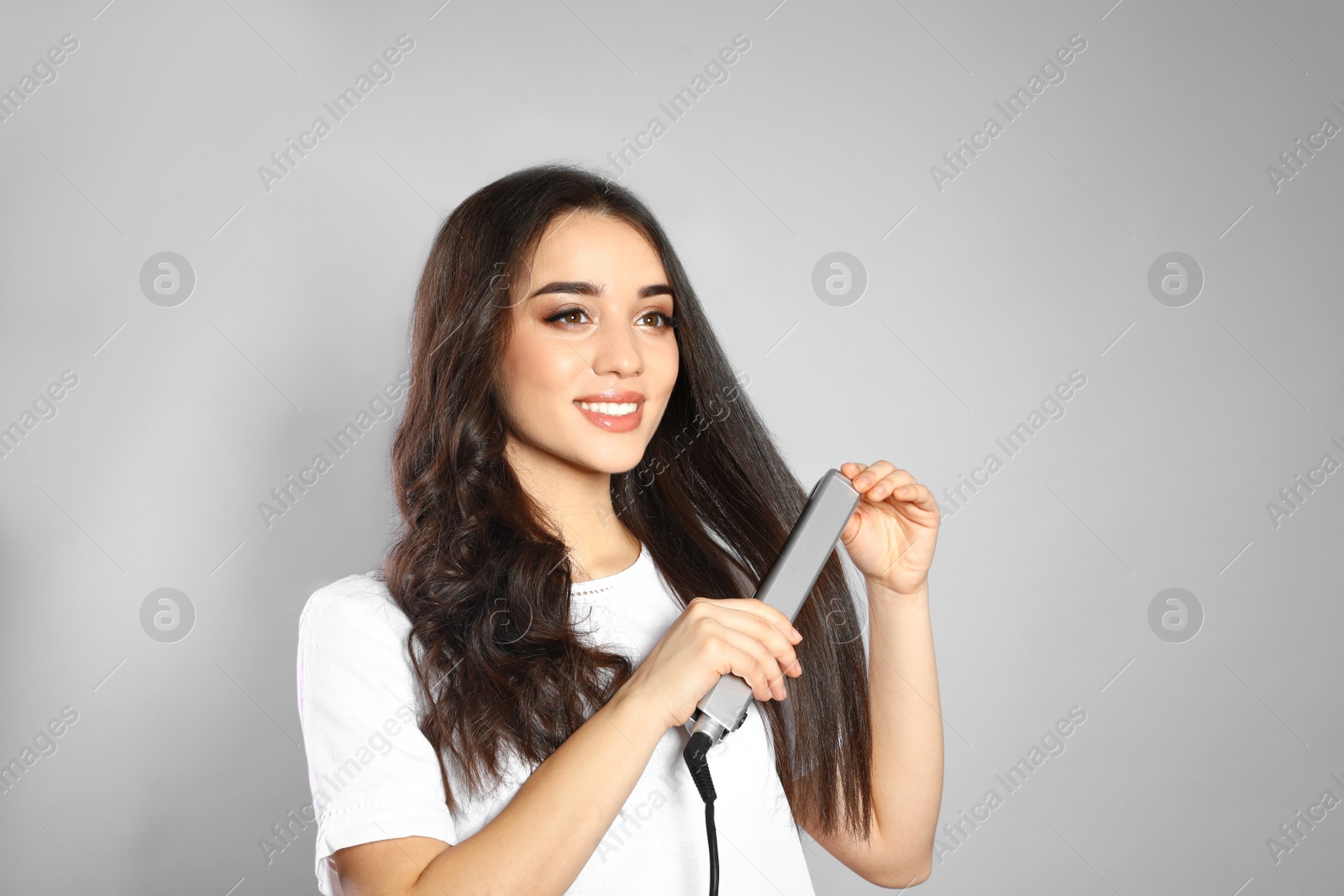 Photo of Happy woman using hair iron on grey background