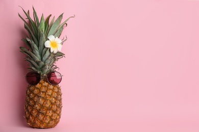 Funny pineapple with sunglasses and plumeria flower on pink background, space for text. Creative concept