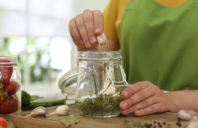 Photo of Woman putting garlic into pickling jar at table in kitchen, closeup