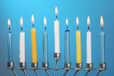 Photo of Hanukkah celebration. Menorah with burning candles on light blue background, closeup