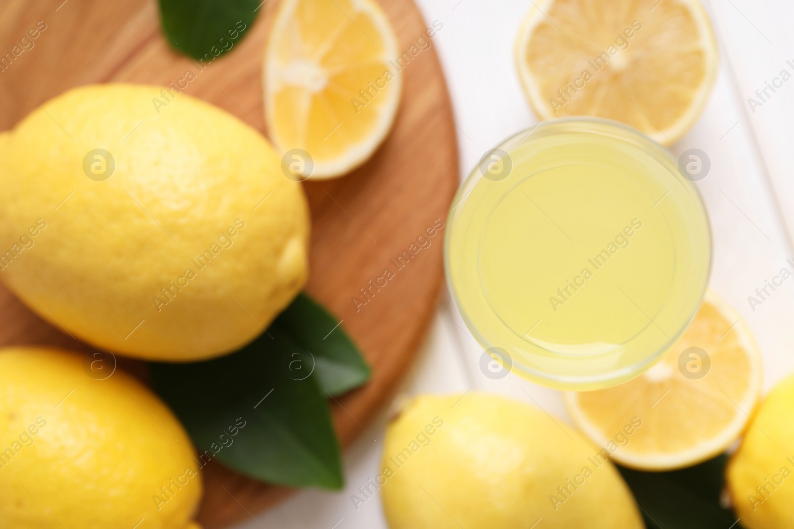 Photo of Liqueur glass with tasty limoncello, lemons and green leaves on table, top view