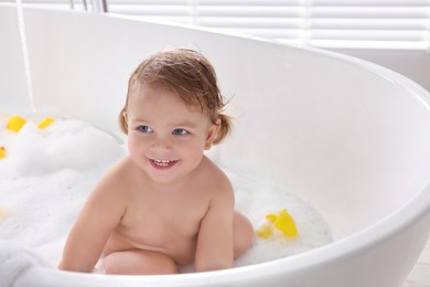 Cute little girl taking bubble bath with toys indoors