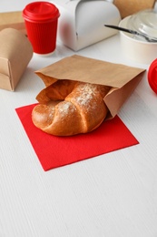 Paper bag with pastry and takeaway food on wooden table. Space for text