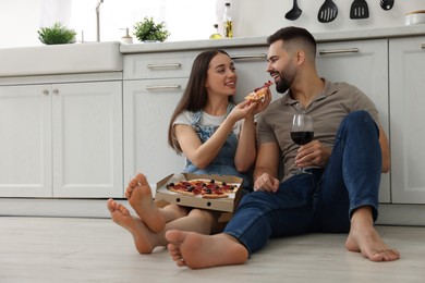 Photo of Happy young couple eating pizza in kitchen. Space for text