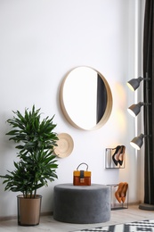 Hallway interior with big round mirror and ottoman chair near white wall