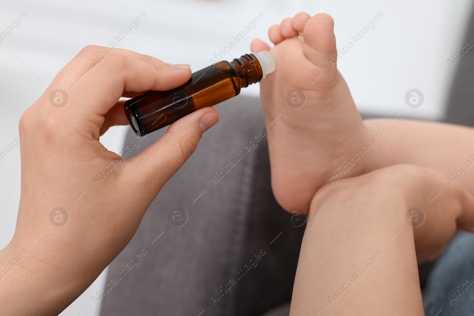 Photo of Mother applying essential oil from roller bottle onto her baby`s heel on blurred background, closeup