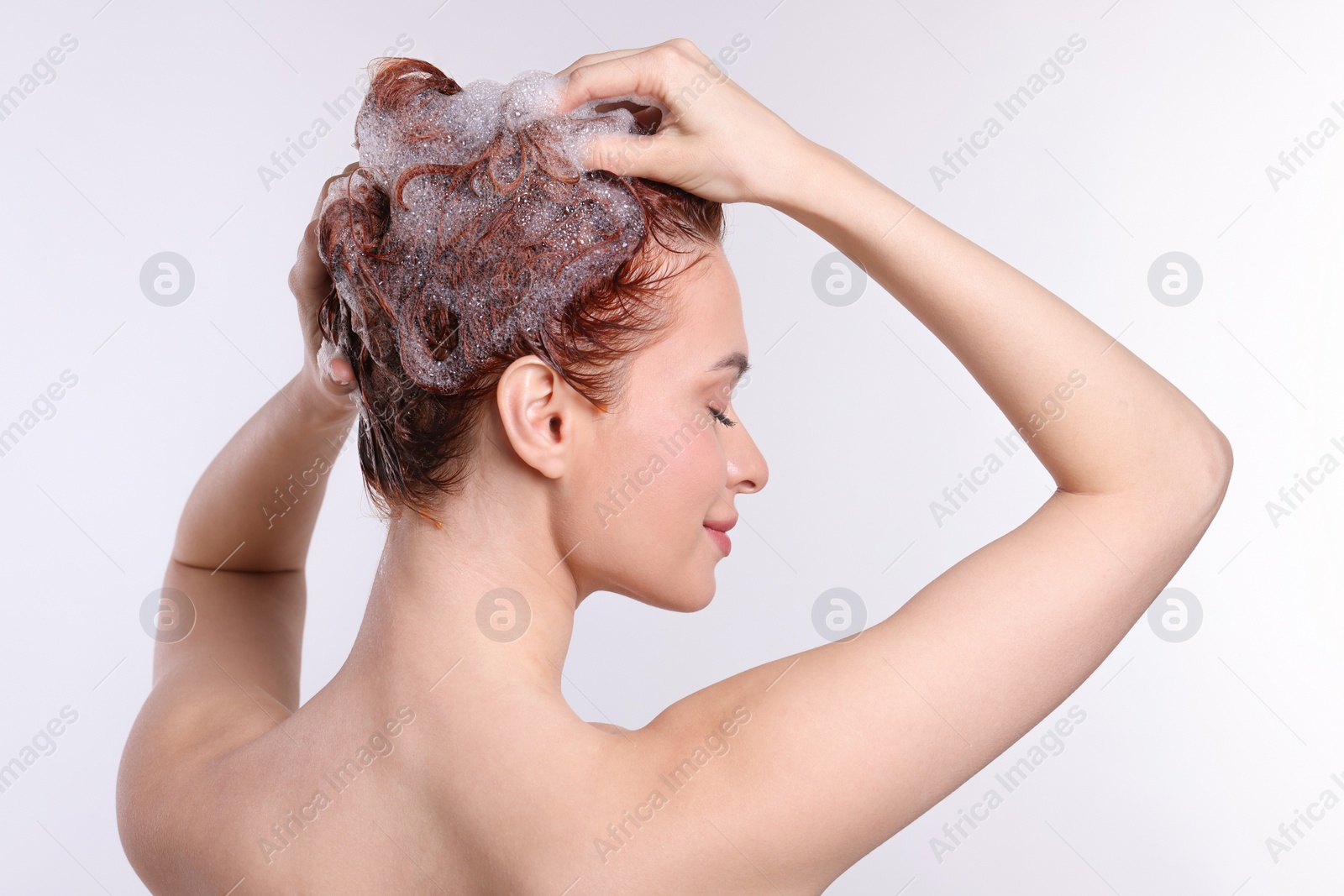 Photo of Young woman washing her hair with shampoo on light grey background, back view