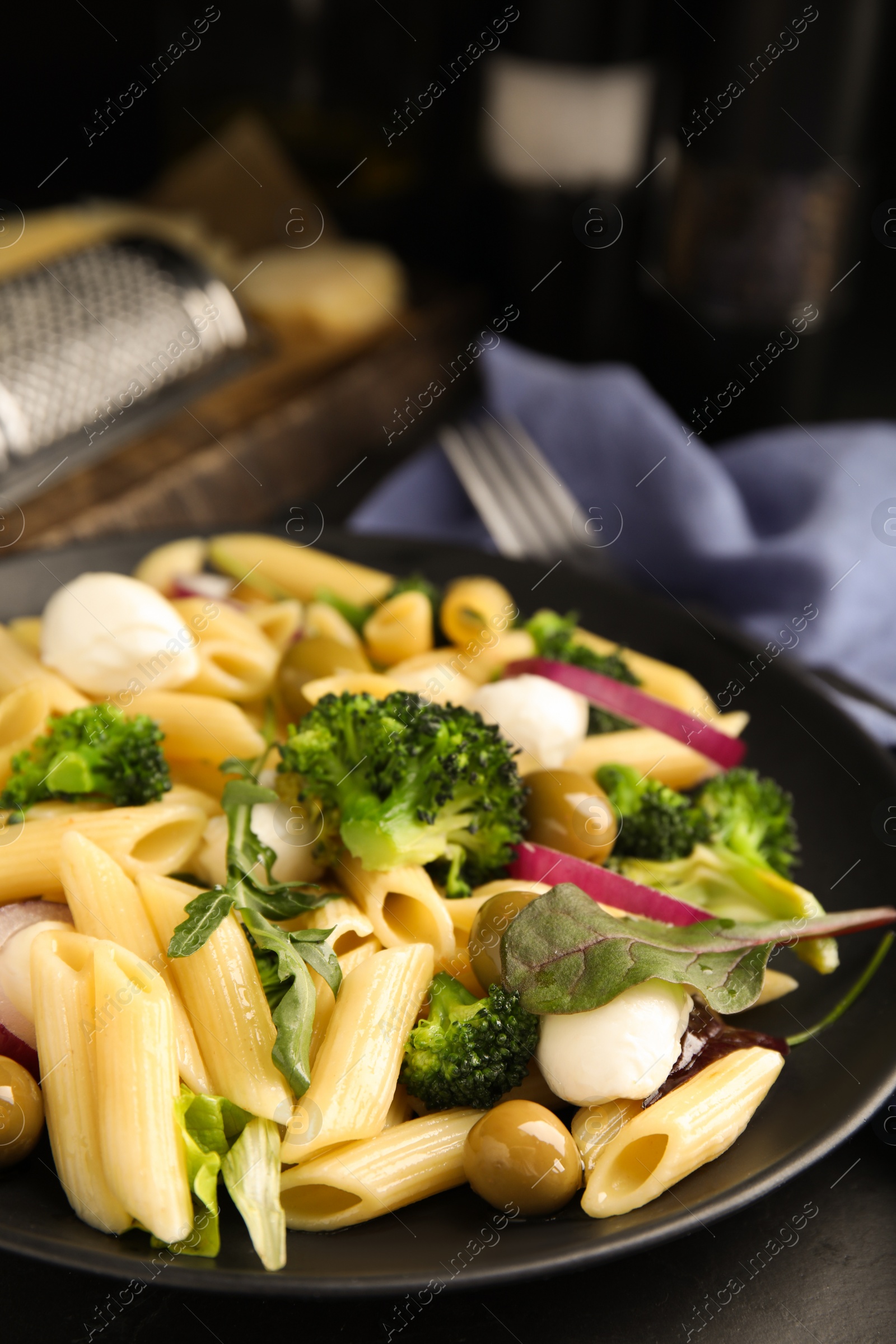Photo of Plate of delicious pasta with broccoli, onion and olives on black table, closeup