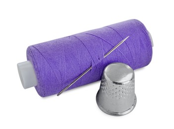 Photo of Thimble and spool of purple sewing thread with needle isolated on white