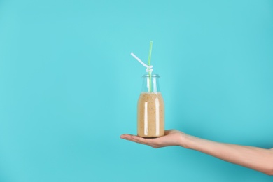 Young woman holding bottle of healthy smoothie on color background