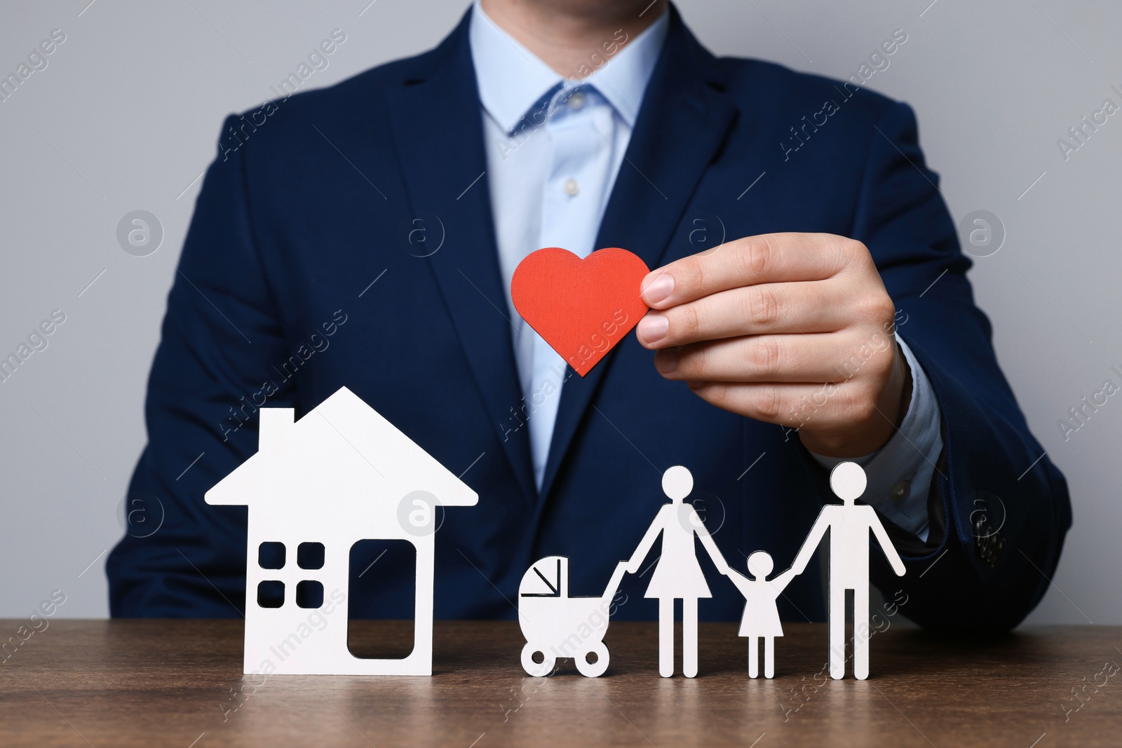 Photo of Man holding figure of heart above family at wooden table. closeup. Insurance concept