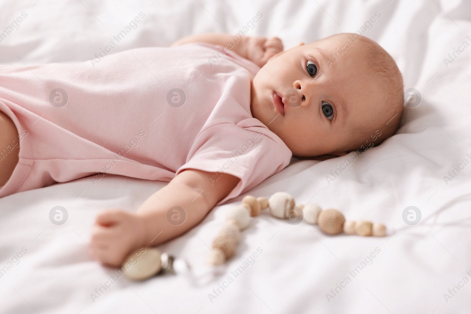 Photo of Cute little baby with toy lying on white sheets