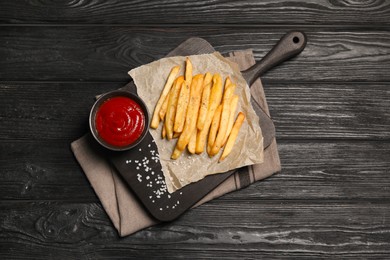 Photo of Delicious fresh french fries and tomato sauce on black wooden table, top view