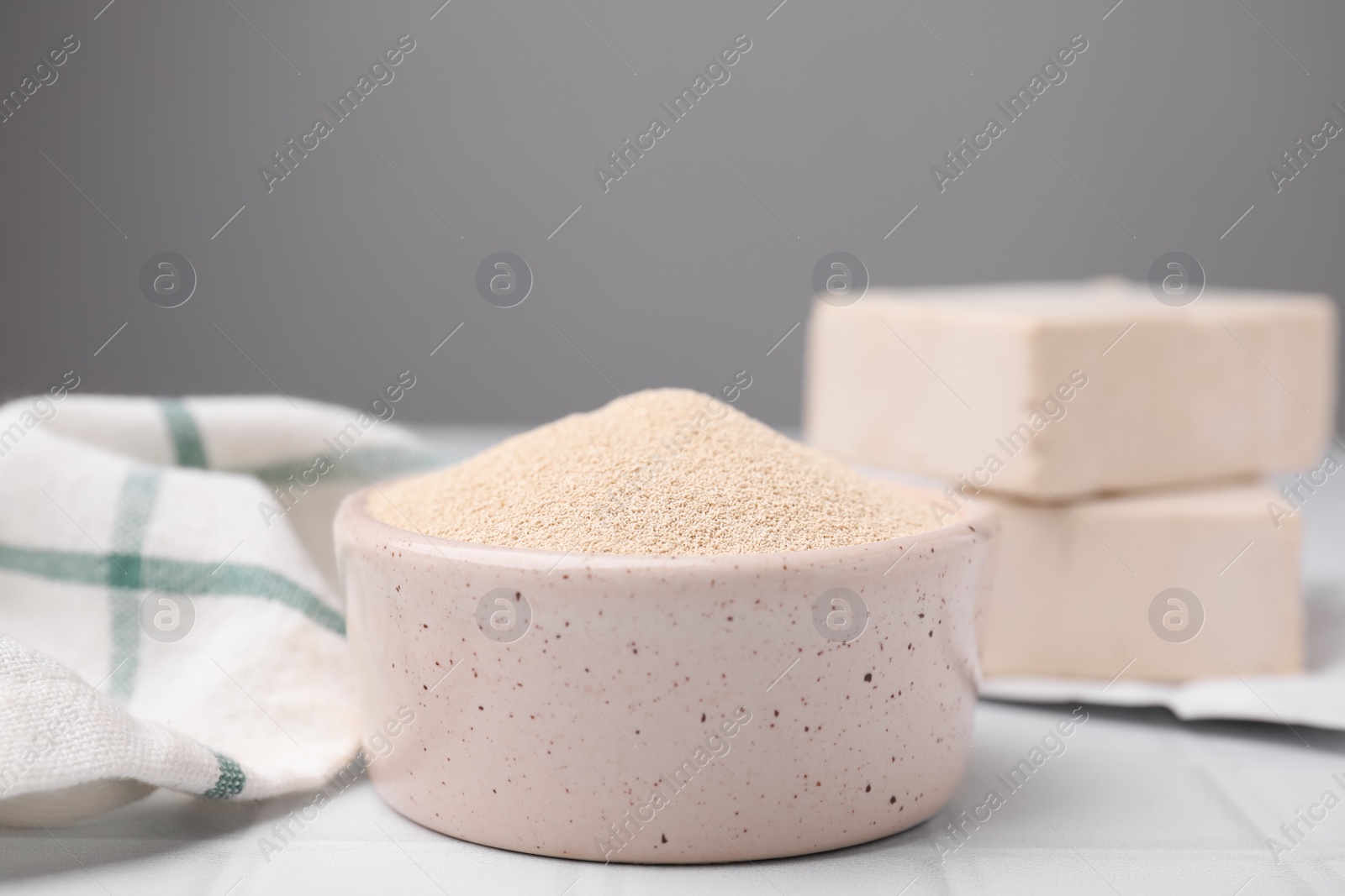 Photo of Granulated yeast in bowl on white tiled table, closeup