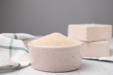 Granulated yeast in bowl on white tiled table, closeup