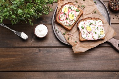 Photo of Delicious sandwiches with radish, egg, cream cheese and microgreens on wooden table, flat lay. Space for text