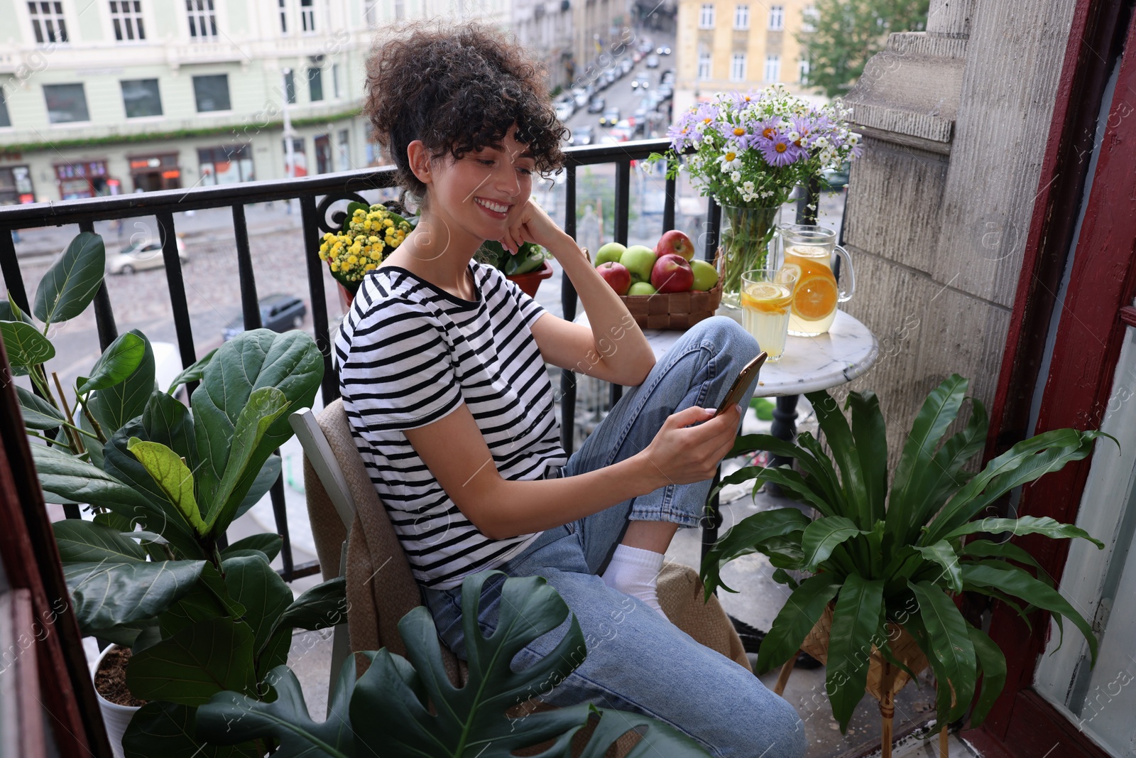 Photo of Beautiful young woman using smartphone at table on balcony with houseplants