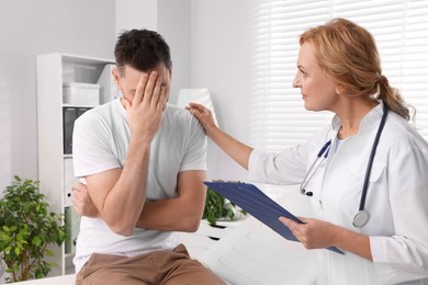 Photo of Doctor with clipboard supporting upset patient in clinic