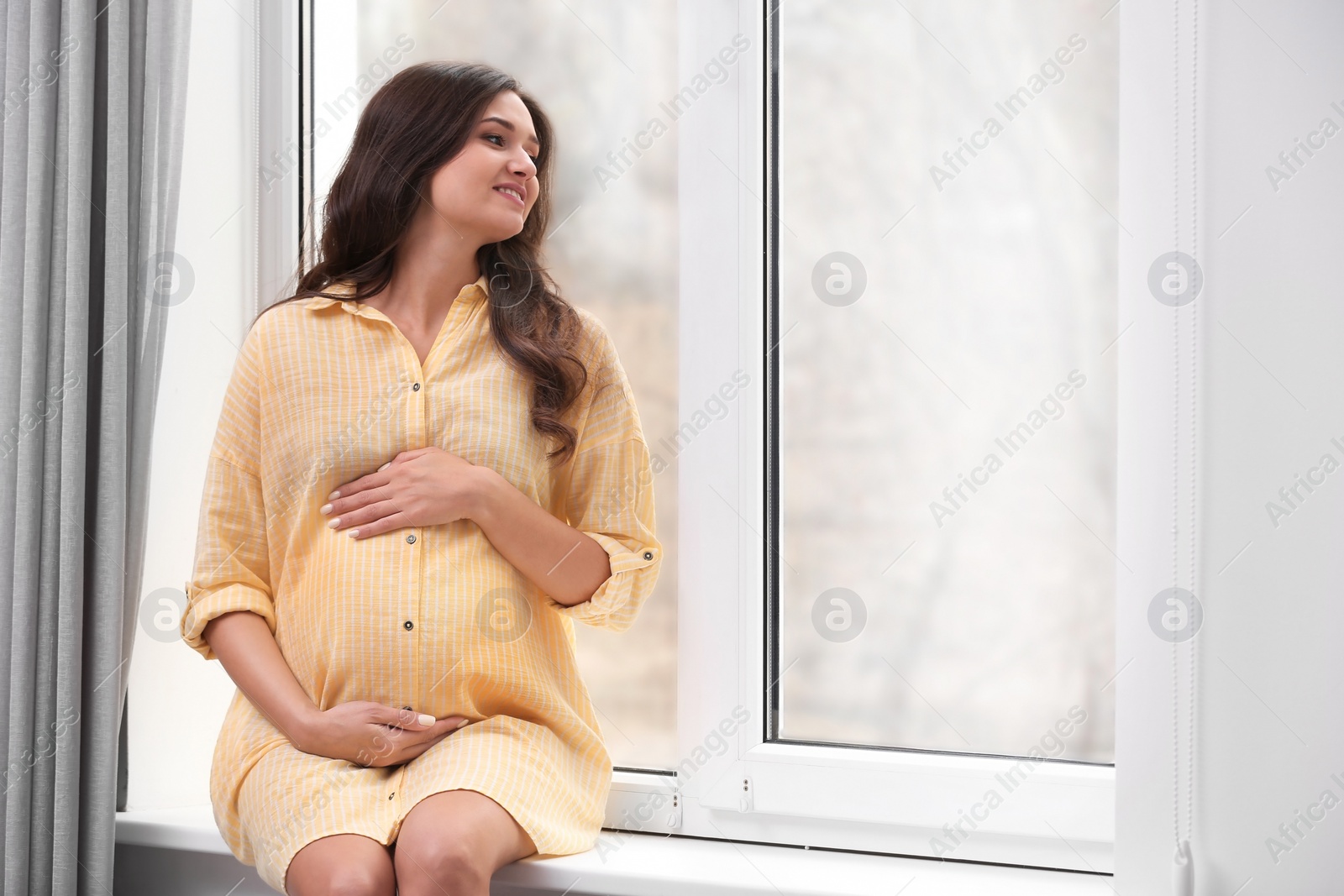 Photo of Beautiful pregnant woman near window at home