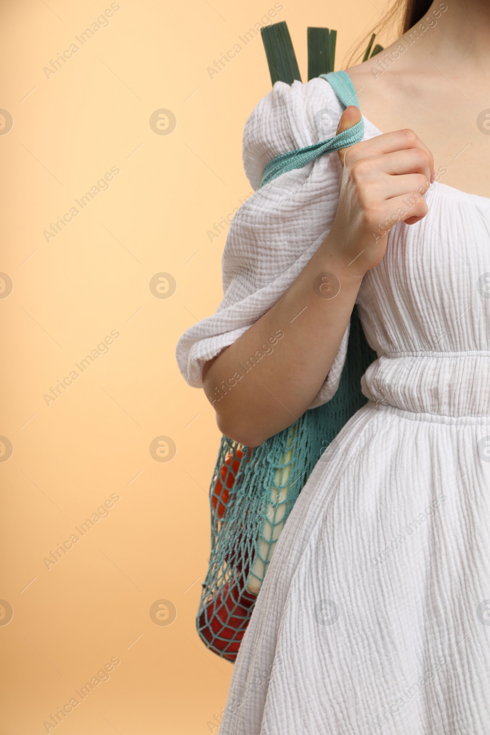 Photo of Woman with string bag of fresh vegetables on beige background, closeup