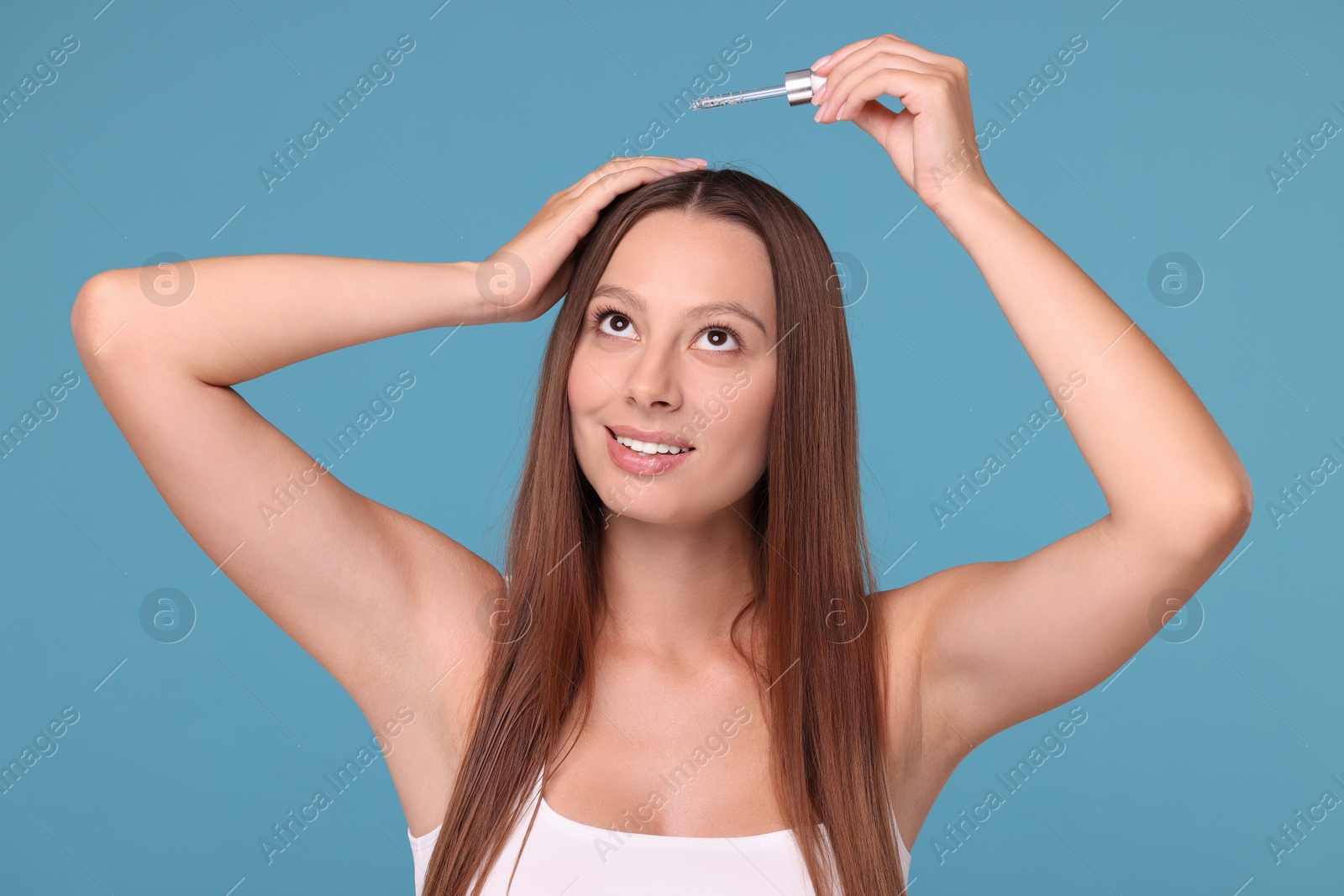 Photo of Beautiful woman applying serum onto hair on light blue background