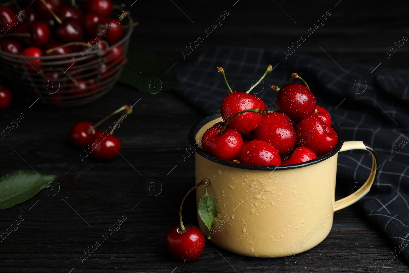 Photo of Metal mug with ripe sweet cherries on dark wooden table. Space for text