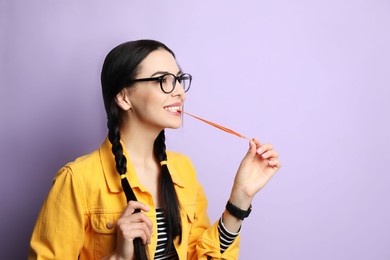 Fashionable young woman with braids chewing bubblegum on lilac background, space for text