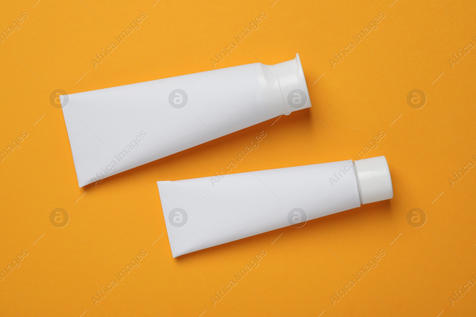 Photo of Blank tubes of toothpaste on orange background, flat lay