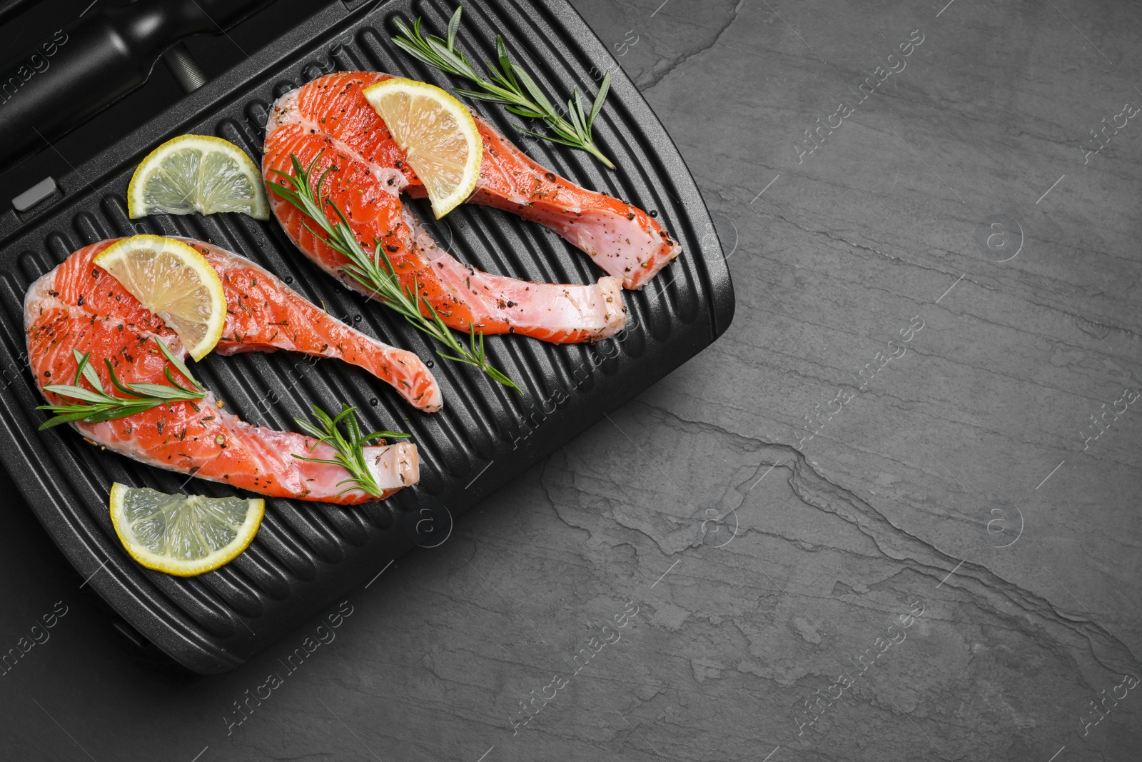 Photo of Cooking salmon. Grill with fresh fish steaks, lemon and rosemary on dark table, top view. Space for text