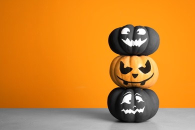 Photo of Pumpkins with scary faces on table against color background, space for text. Halloween decor