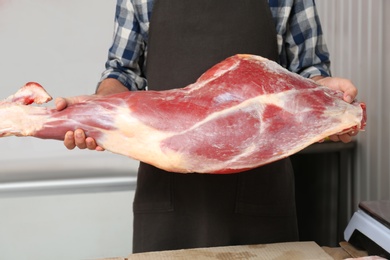 Male butcher holding fresh raw meat in shop, closeup