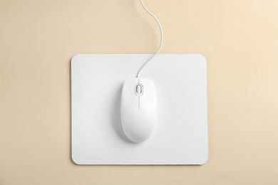 Photo of Modern wired optical mouse and pad on beige background, top view
