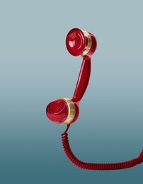 Image of Handset of vintage red corded telephone flying in air on light blue background