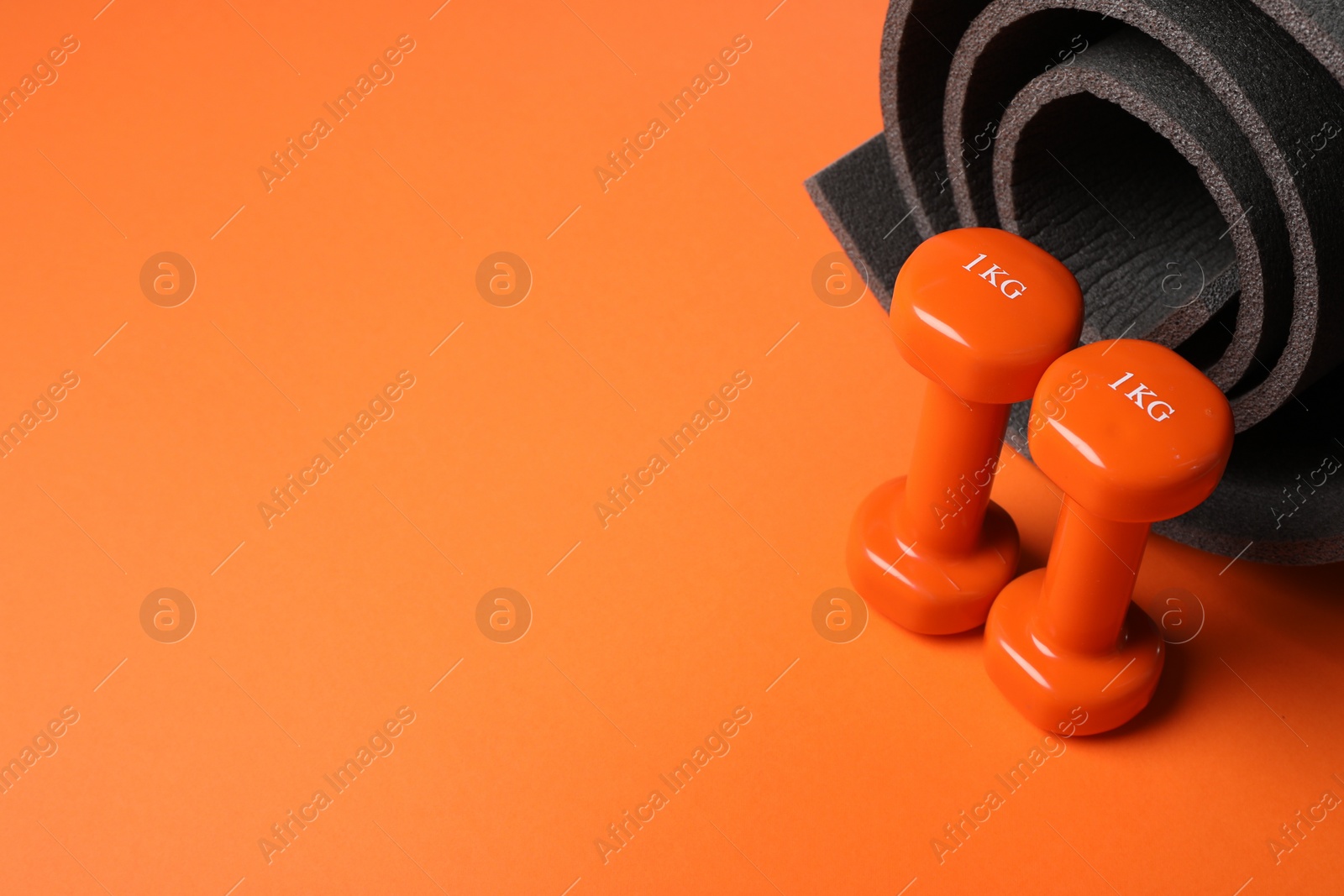 Photo of Dumbbells and yoga mat on orange background. Space for text