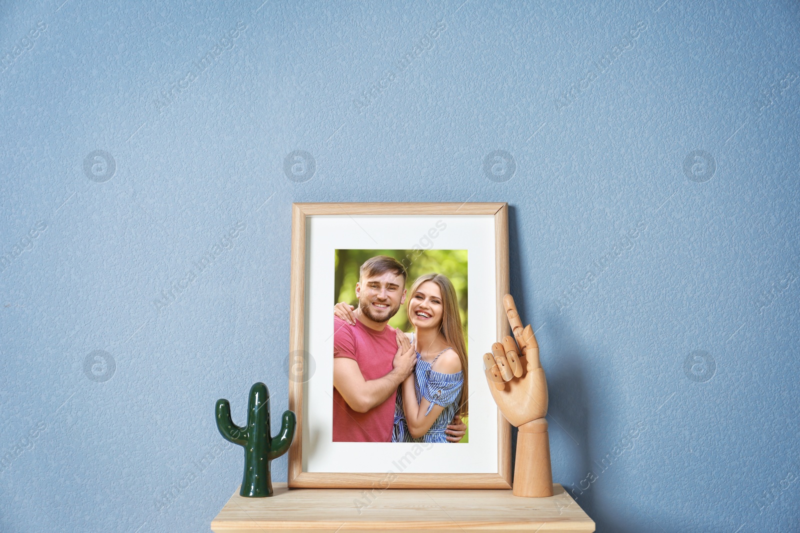 Image of Portrait of happy young couple in photo frame on table near light blue wall