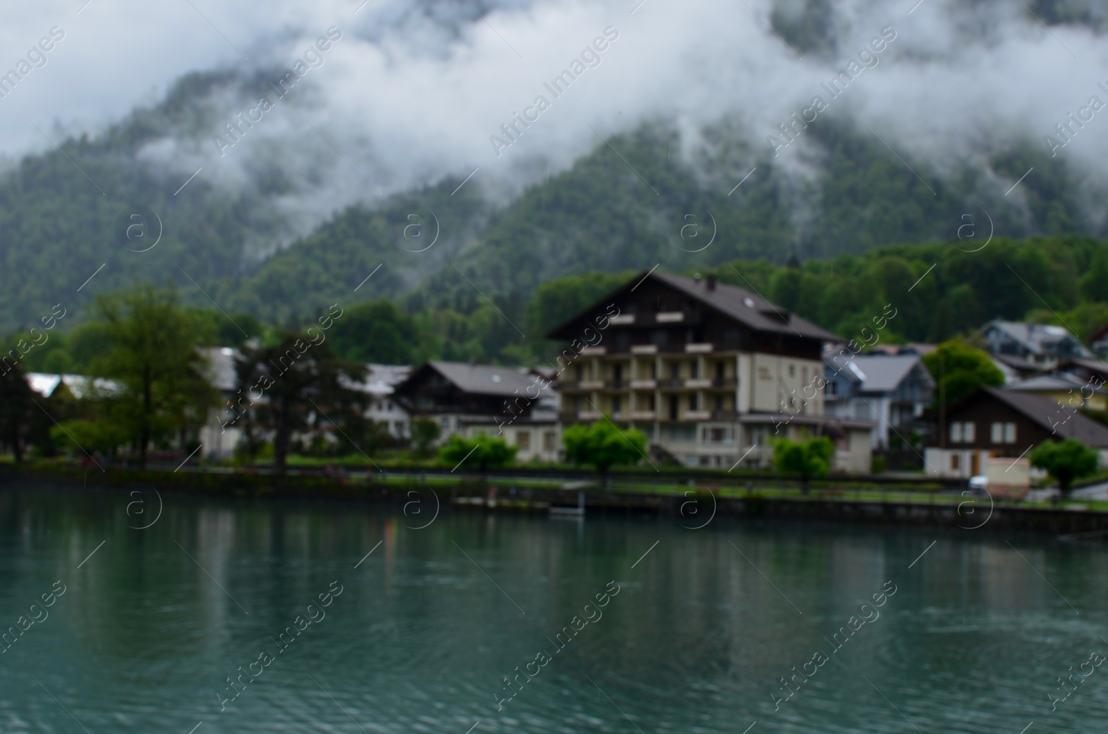 Photo of Blurred view of beautiful village on lake shore near mountains