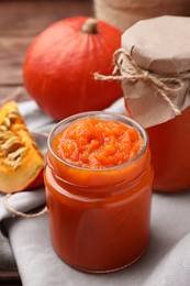 Jars of pumpkin jam and fresh pumpkins on wooden table, closeup