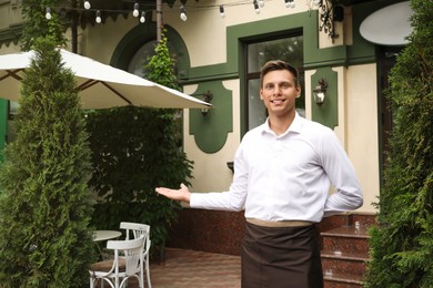 Photo of Happy young waiter in uniform near cafe