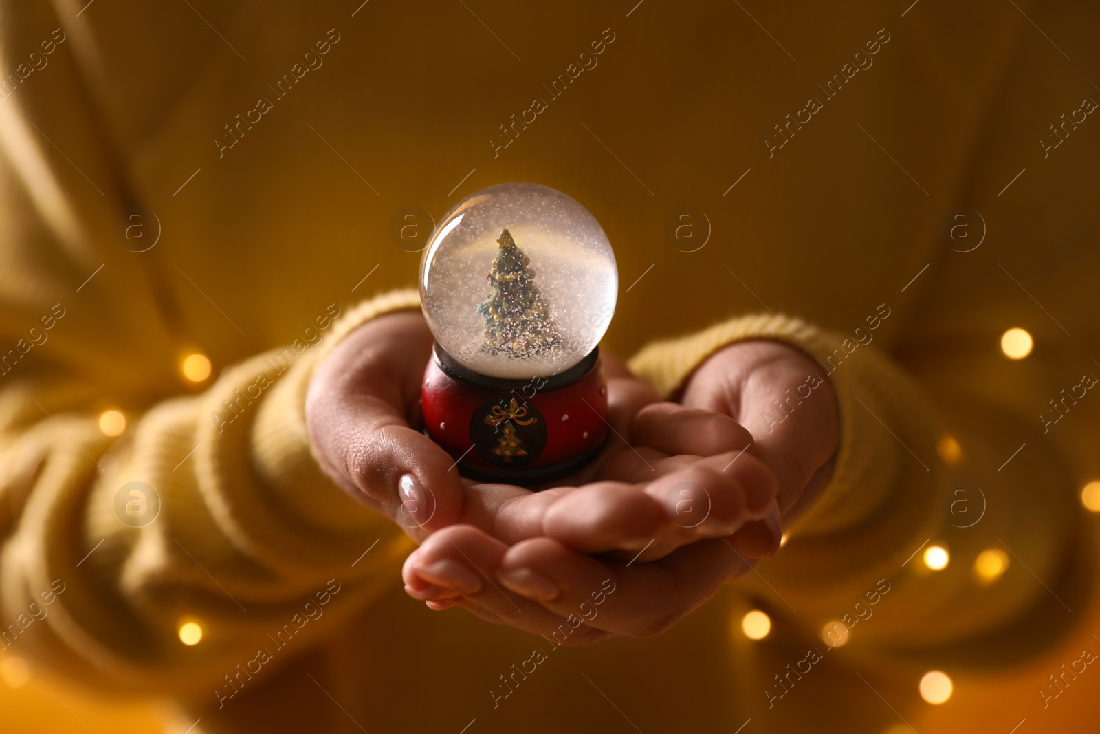 Photo of Woman in yellow sweater holding decorative snow globe, closeup