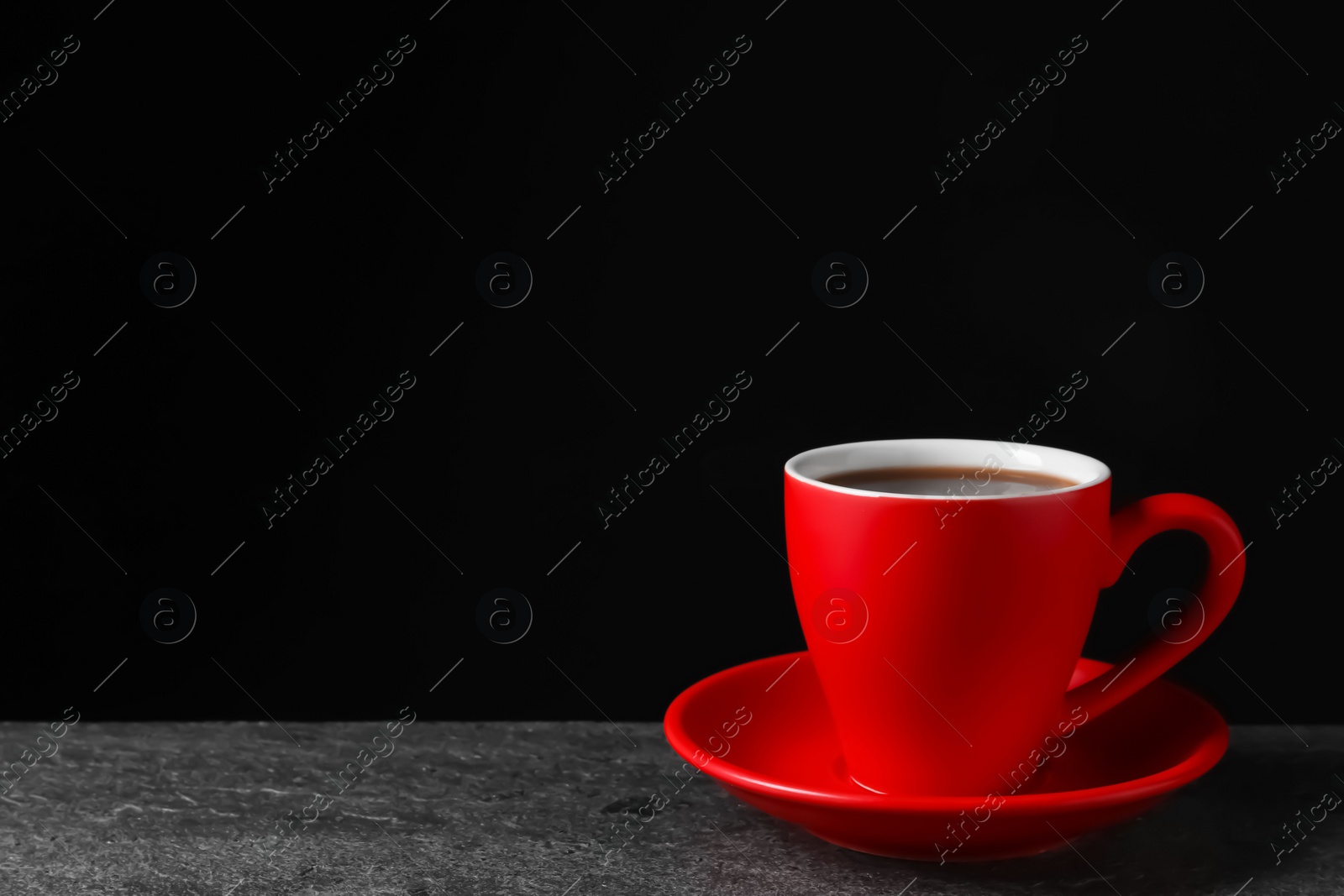 Photo of Red cup with aromatic coffee on grey textured table against black background. Space for text