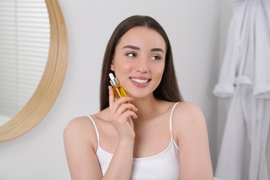 Happy young woman with bottle of essential oil in bathroom